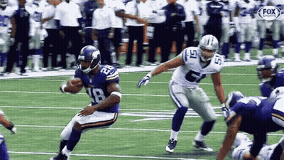 Man With Headphones And Hat In Front Of Football Players GIF