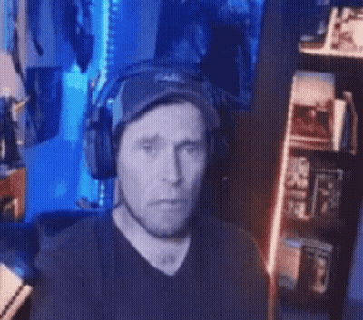 Man With Headphones And Hat Sitting In Front Of Bookshelf GIF