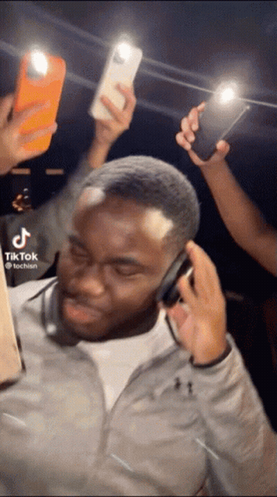 Man With Headphones Surrounded By People Holding Phones GIF