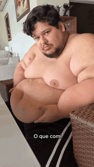 Man With Large Belly Sitting On Wicker Chair Saying O Que Comi GIF