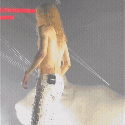Man With Long Blonde Hair In White Lace Up Pants With Microphone GIF