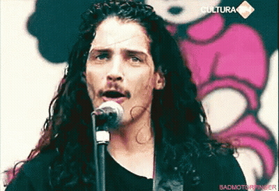Man With Long Curly Hair And Mustache Singing Into Microphone GIF