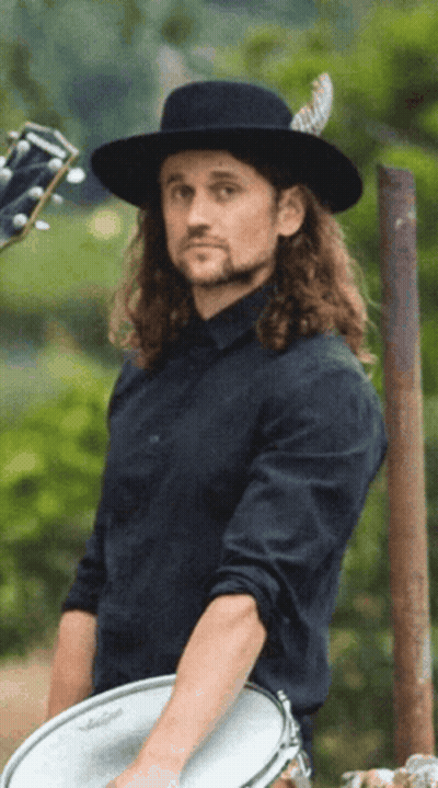 Man With Long Hair And Black Hat Holding Drum GIF