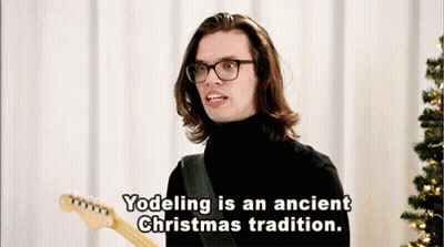 Man With Long Hair And Glasses Holding Guitar Says Yodeling Is An Ancient Christmas Tradition GIF