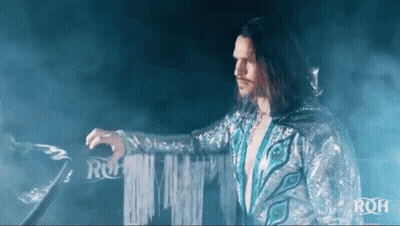 Man With Long Hair And Peacock Feather Costume Standing In Ring GIF