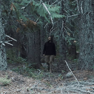 Man With Long Hair Walking Through Dark Forest GIF