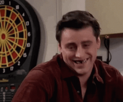 Man With Missing Teeth Smiling in Front of Dart Board