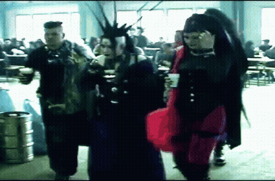 Man With Mohawk And Woman In Red Dress Walking In Crowded Room GIF