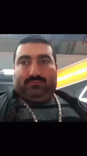 Man With Mustache And Chain Looking At Camera GIF