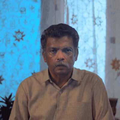 Man With Mustache Looking At Camera In Front Of Blue Curtain GIF