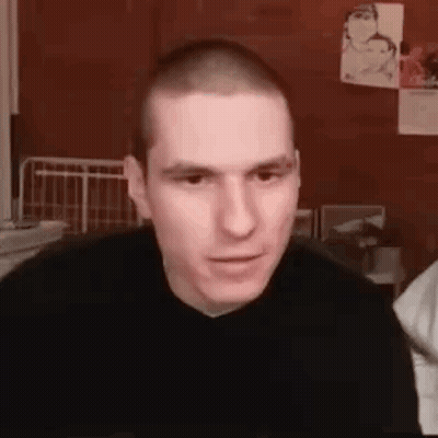 Man With Shaved Head In Black Sweater Looking At Camera GIF