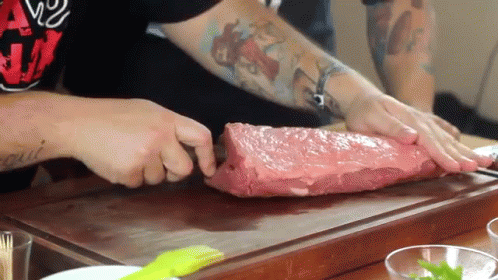Man With Tattoo Cutting Large Piece Of Meat GIF