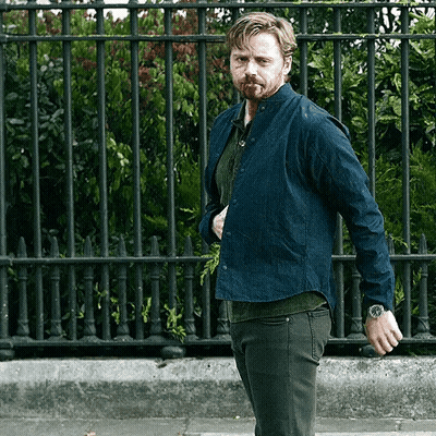 Man With Watch Standing In Front Of Metal Fence GIF