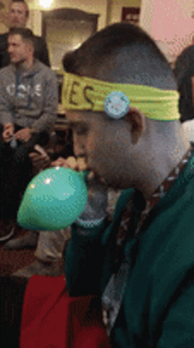 Man With Yes Headband Blowing Up Green Balloon GIF