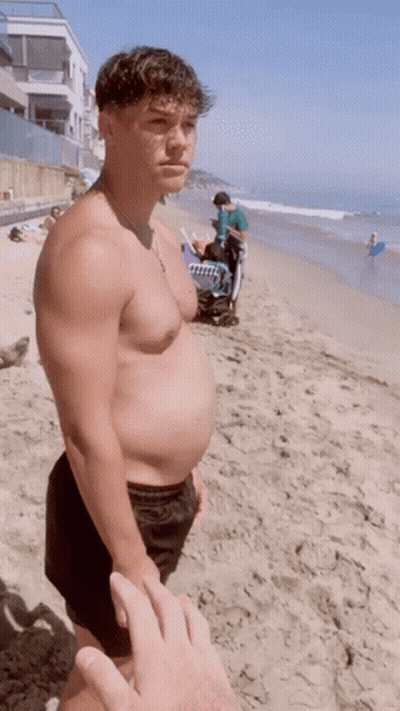 Man Without Shirt Holding Towel On Beach GIF