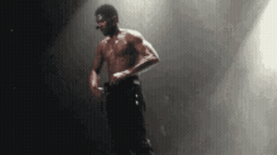 Man Without Shirt Standing At Microphone On Stage GIF