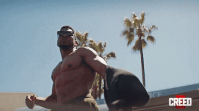 Man Without Shirt Standing In Front Of Creed Building GIF