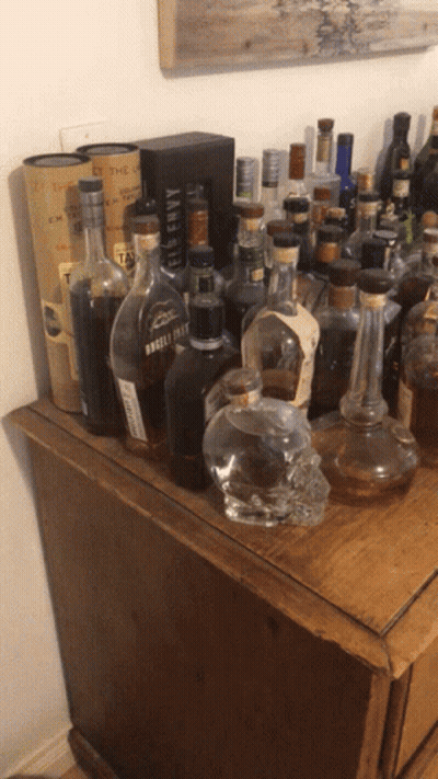 Many Bottles Of Liquor Are On A Wooden Table Including A Bottle Of Whiskey Called Kentucky Straight GIF