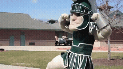 Mascot In Spartan Costume In Front Of Brick Building GIF
