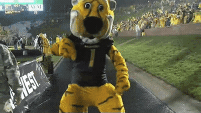 Mascot In Tiger Costume Dancing In Front Of West Sign GIF