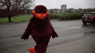 Mascot Walking Down Street In Front Of Parking Lot GIF