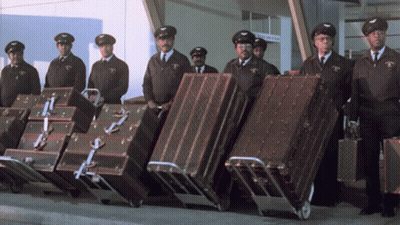 Men Carrying Luggage With Arrivals & Departures Sign GIF