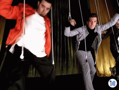 Men Dancing In Front Of Yellow Curtain With Letter N GIF