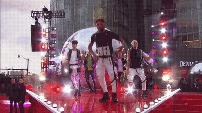 Men Dancing On Stage In Front Of Devil's Building GIF