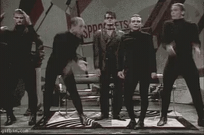 Men In Black Jumpsuits Dancing On Stage GIF