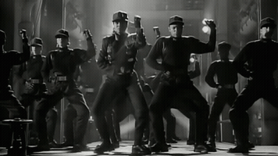 Men In Black Uniforms Dancing On Stage GIF