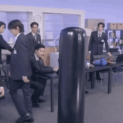 Men In Suits Standing Around Punching Bag GIF