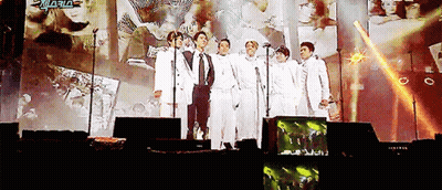 Men Standing On Stage With Microphones In Front Of Screen Saying Aria GIF
