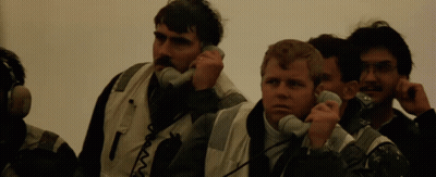 Men Talking On Telephones With Letter T On Jacket GIF