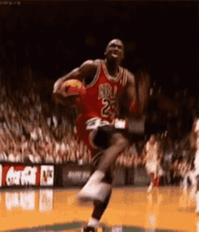 Michael Jordan Is Jumping In The Air While Holding A Basketball In His Hands . GIF