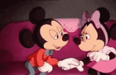 Mickey Mouse And Minnie Mouse Are Standing Next To Each Other On A Pink Couch Holding Hands . GIF