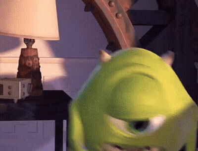 Mike Wazowski From Monsters Inc Is Standing In Front Of A Lamp On A Table GIF