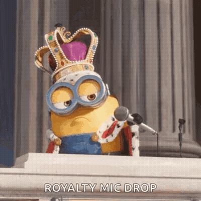 Minion Wearing Crown And Goggles Sitting At Podium Holding Microphone GIF