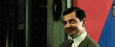 Mr Bean In Suit And Tie Smiling In Front Of Red And Blue Wall GIF