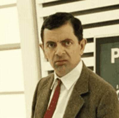 Mr Bean Is Wearing A Suit And Tie And Is Looking At The Camera . GIF