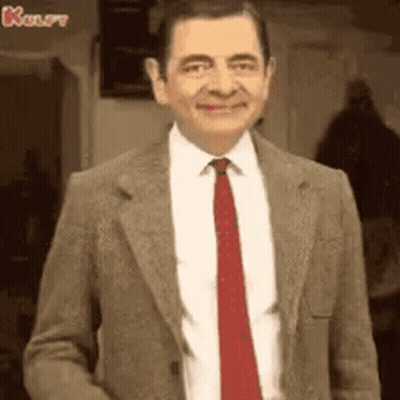 Mr Bean Is Wearing A Suit And Tie And Smiling At The Camera . GIF