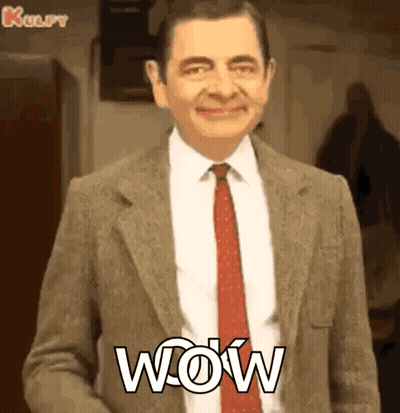 Mr Bean Is Wearing A Suit And Tie And Smiling With The Word Wow Written On His Chest . GIF