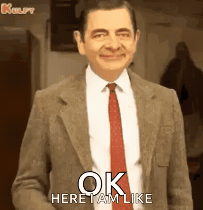 Mr Bean Smiling In Suit And Tie Saying Ok Here I Am GIF