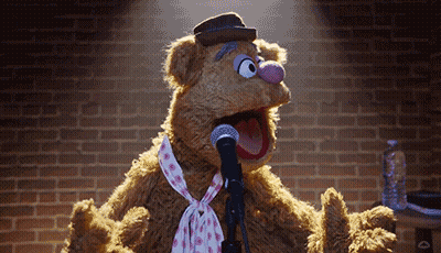 Muppet Fozzie Bear Singing Into A Microphone With A Brick Wall In The Background GIF