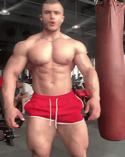 Muscular Man In Red Shorts Next To Punching Bag GIF
