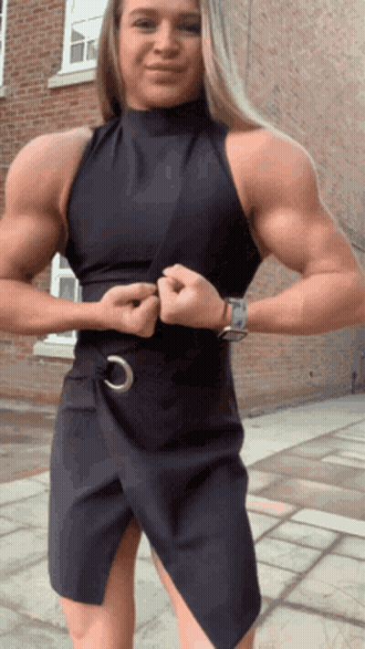 Muscular Woman In Black Dress In Front Of Brick Building GIF