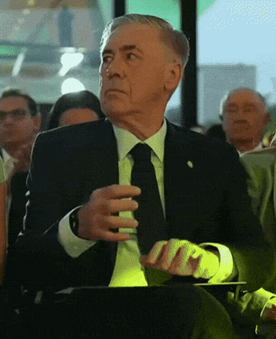 Older Man In Suit And Tie Sitting In Crowd GIF