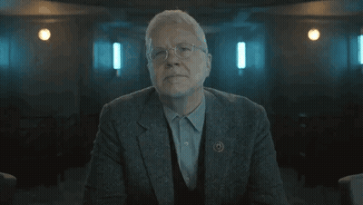 Older Man In Suit Arms Crossed Dark Room GIF