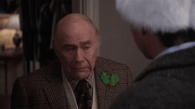 Older Man In Suit Talking To Man In Santa Hat GIF