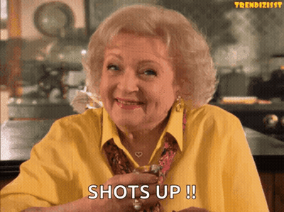 Older Woman In Yellow Holding Shot Glass Says Shots Up GIF