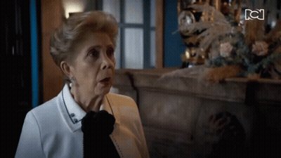 Older Woman Sitting By Fireplace With Clock GIF